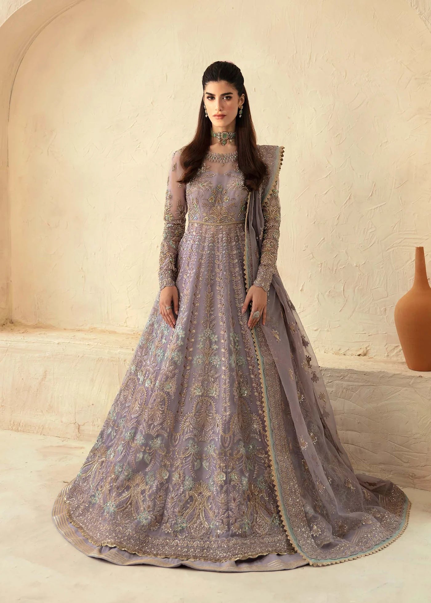Woman in a gray embroidered gown standing against a beige wall.