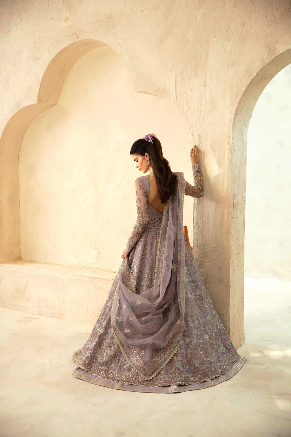 Woman in a traditional embroidered dress standing in a sunlit room with arches.