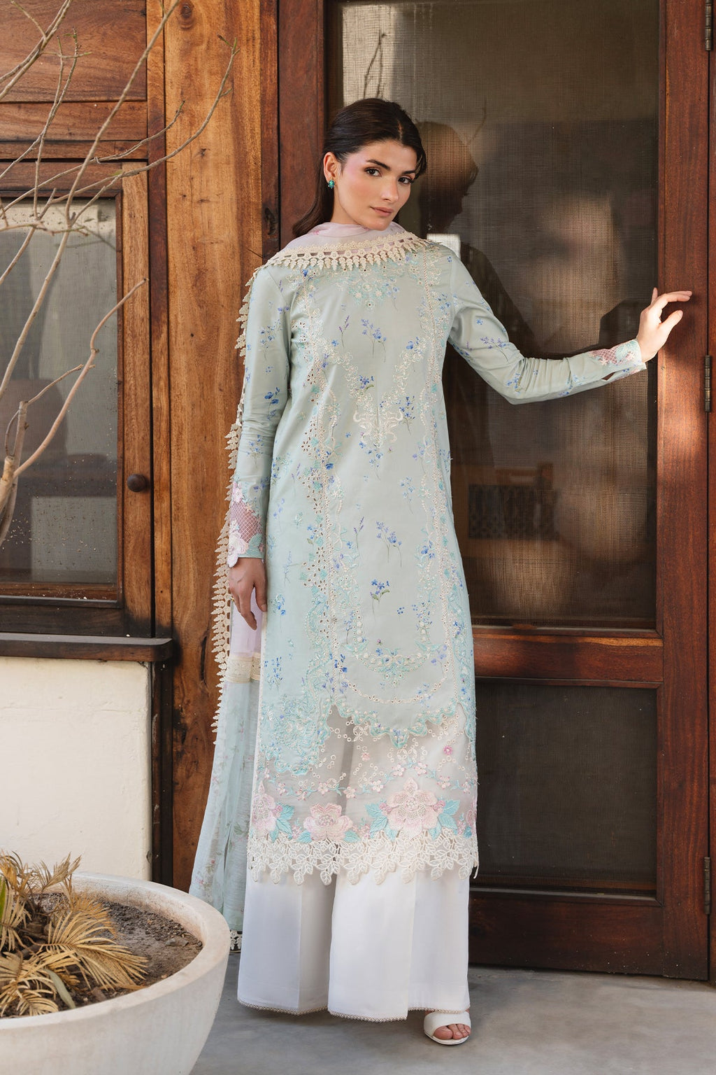 Woman in a light blue floral dress standing indoors next to a wooden door.