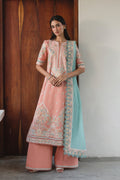Woman wearing a traditional outfit with a pink and blue color scheme against a wooden and white wall.
