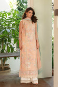 Woman wearing a peach-colored embroidered traditional outfit in an outdoor setting with plants.