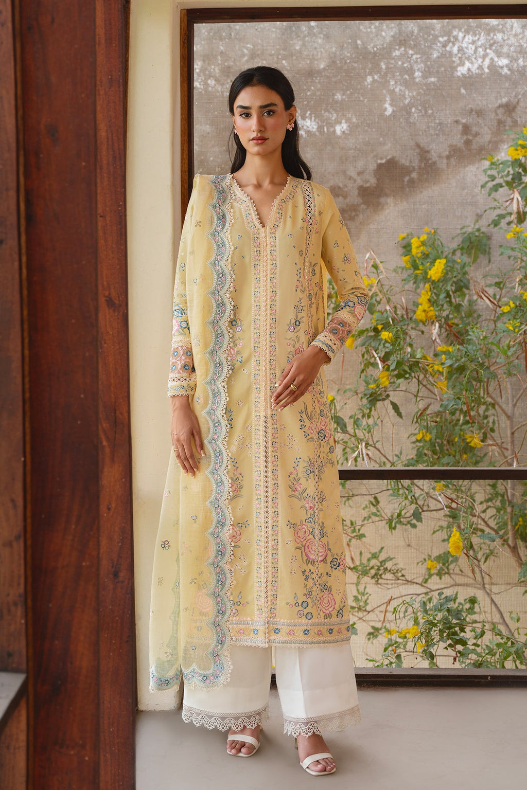 Woman in a yellow embroidered outfit standing in front of a floral wall mural.
