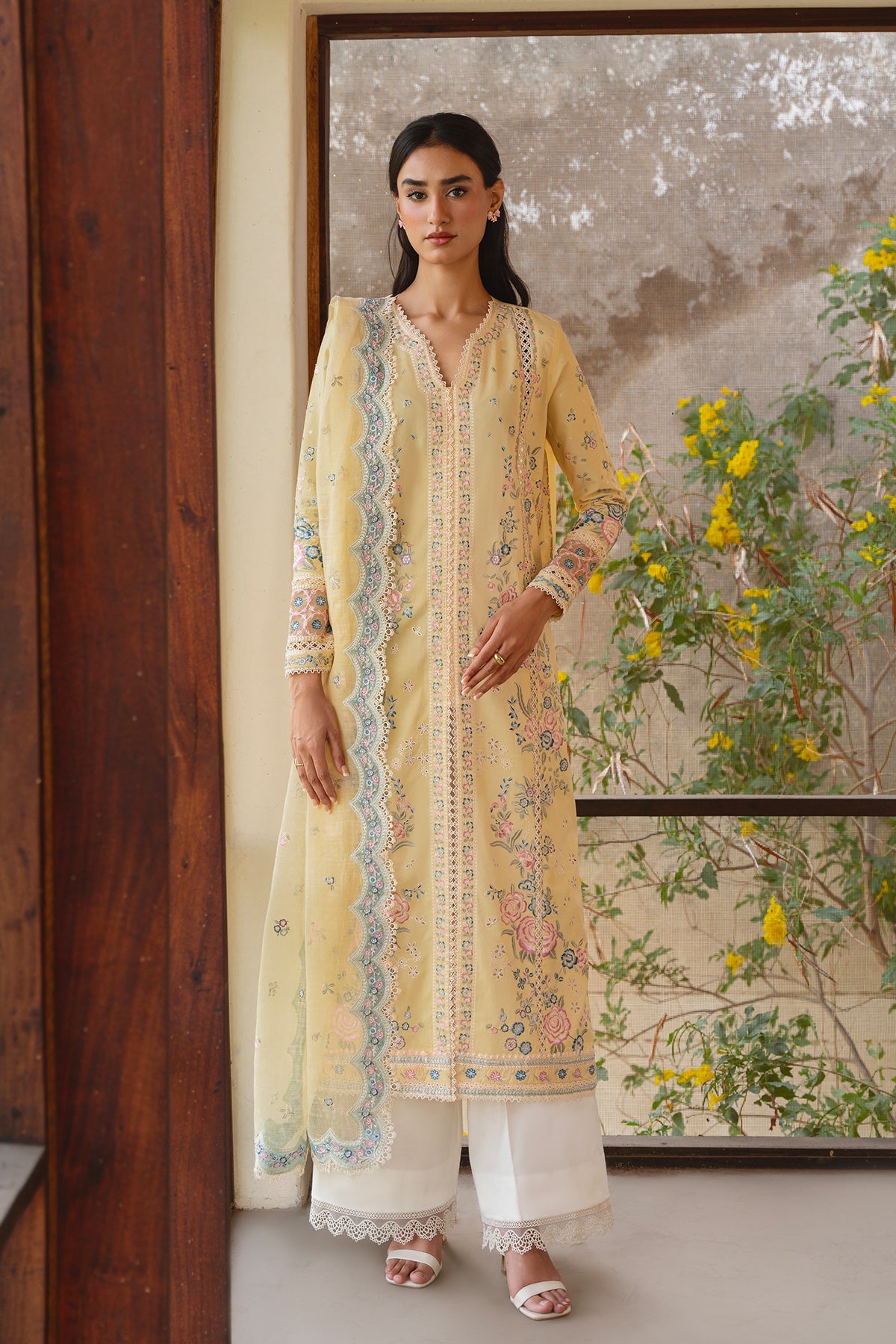 Woman in a yellow embroidered outfit standing in front of a floral wall mural.