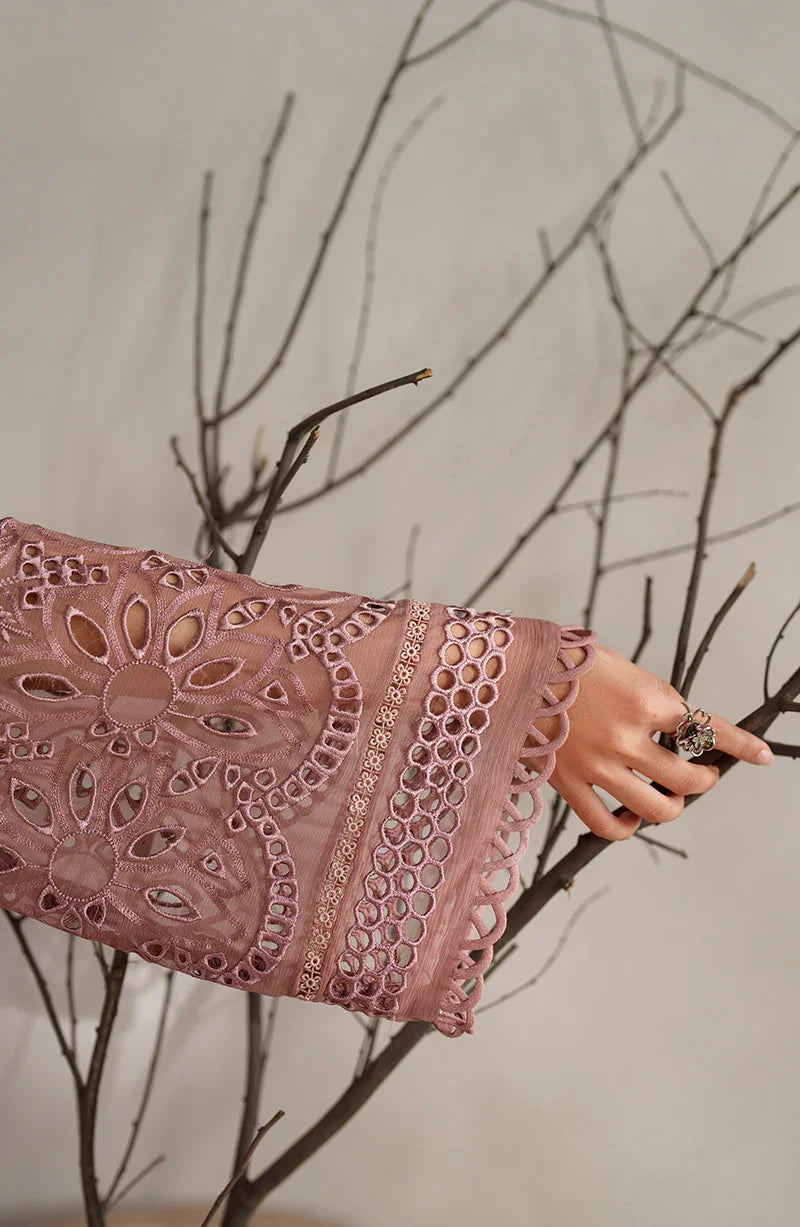 Close-up of a hand holding a pink lace fabric against a neutral background with branches.