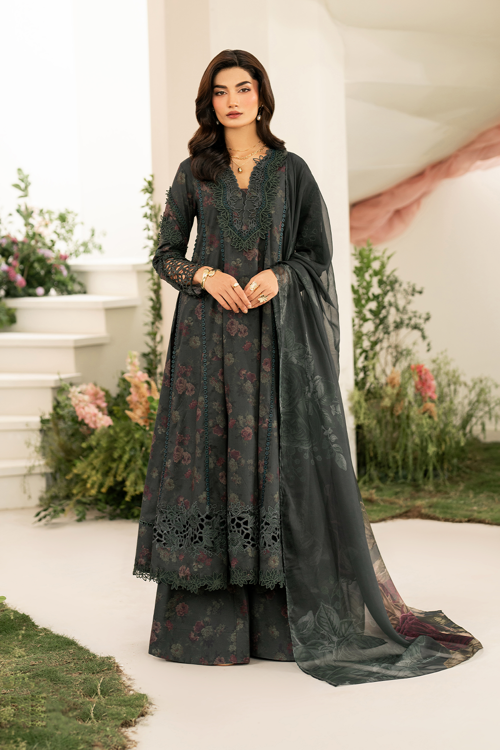 Woman wearing a dark green traditional outfit with floral patterns in an outdoor setting.