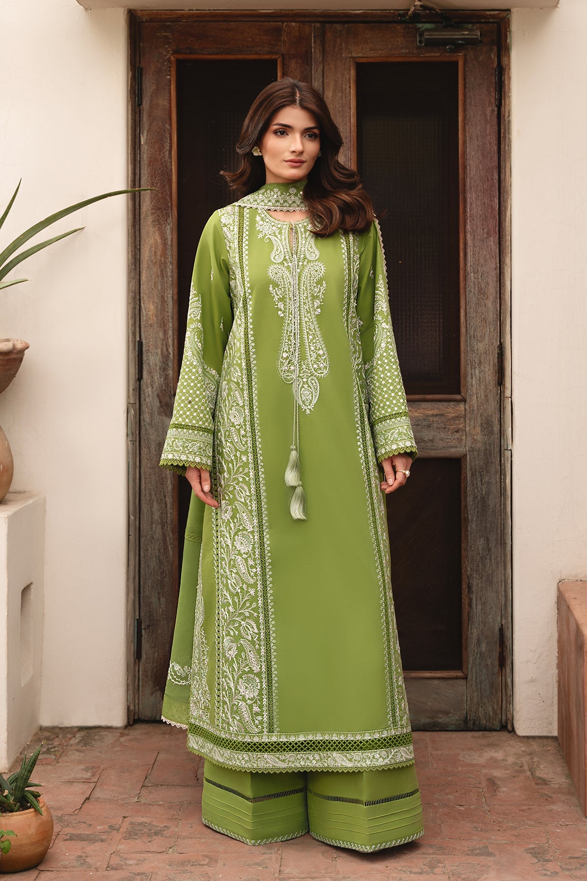 Woman wearing a green embroidered traditional outfit standing in front of a wooden door.