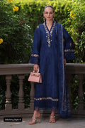 Woman in a blue embroidered dress standing outdoors with greenery in the background