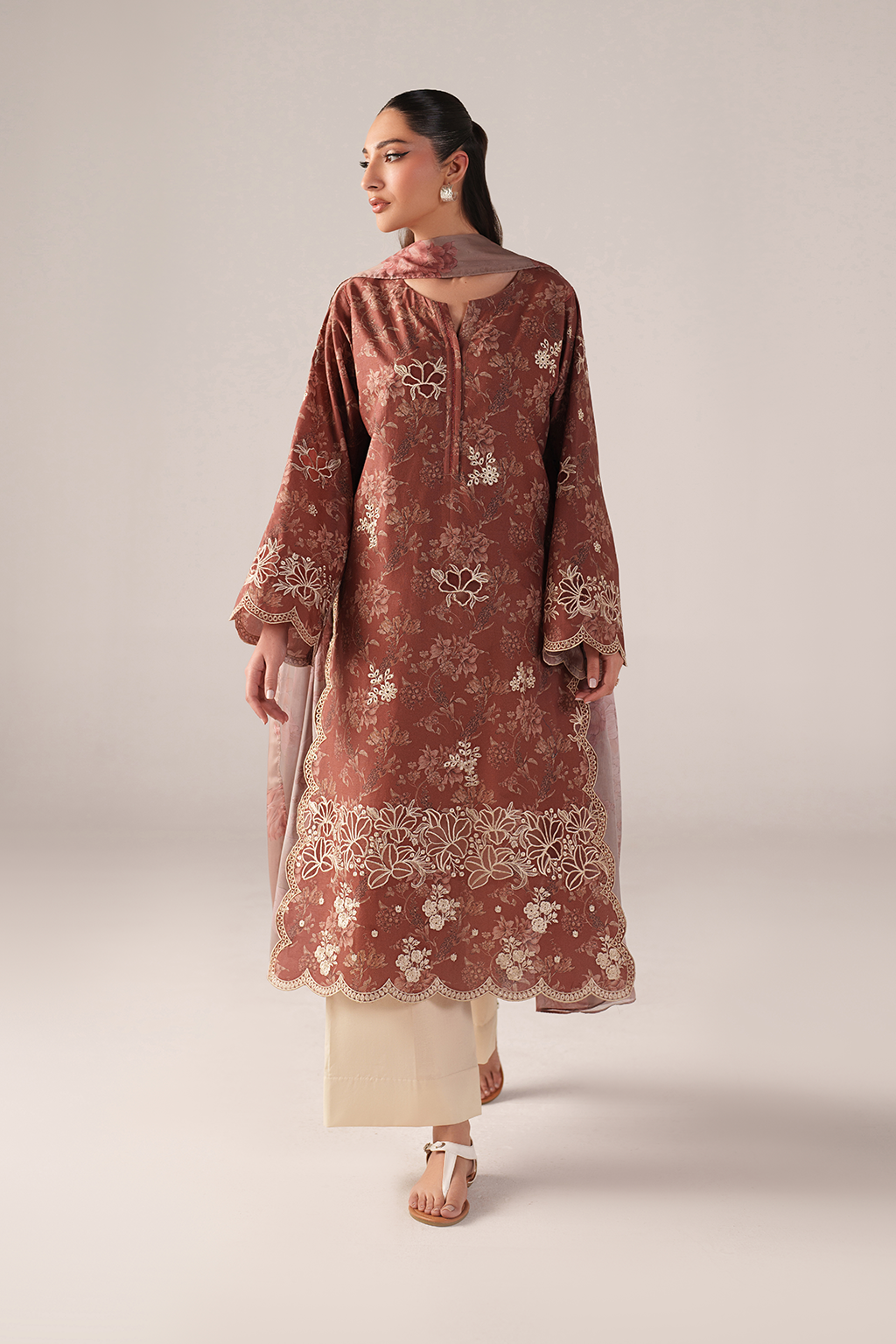 Woman wearing a rust-colored embroidered kurta with white pants on a light gray background