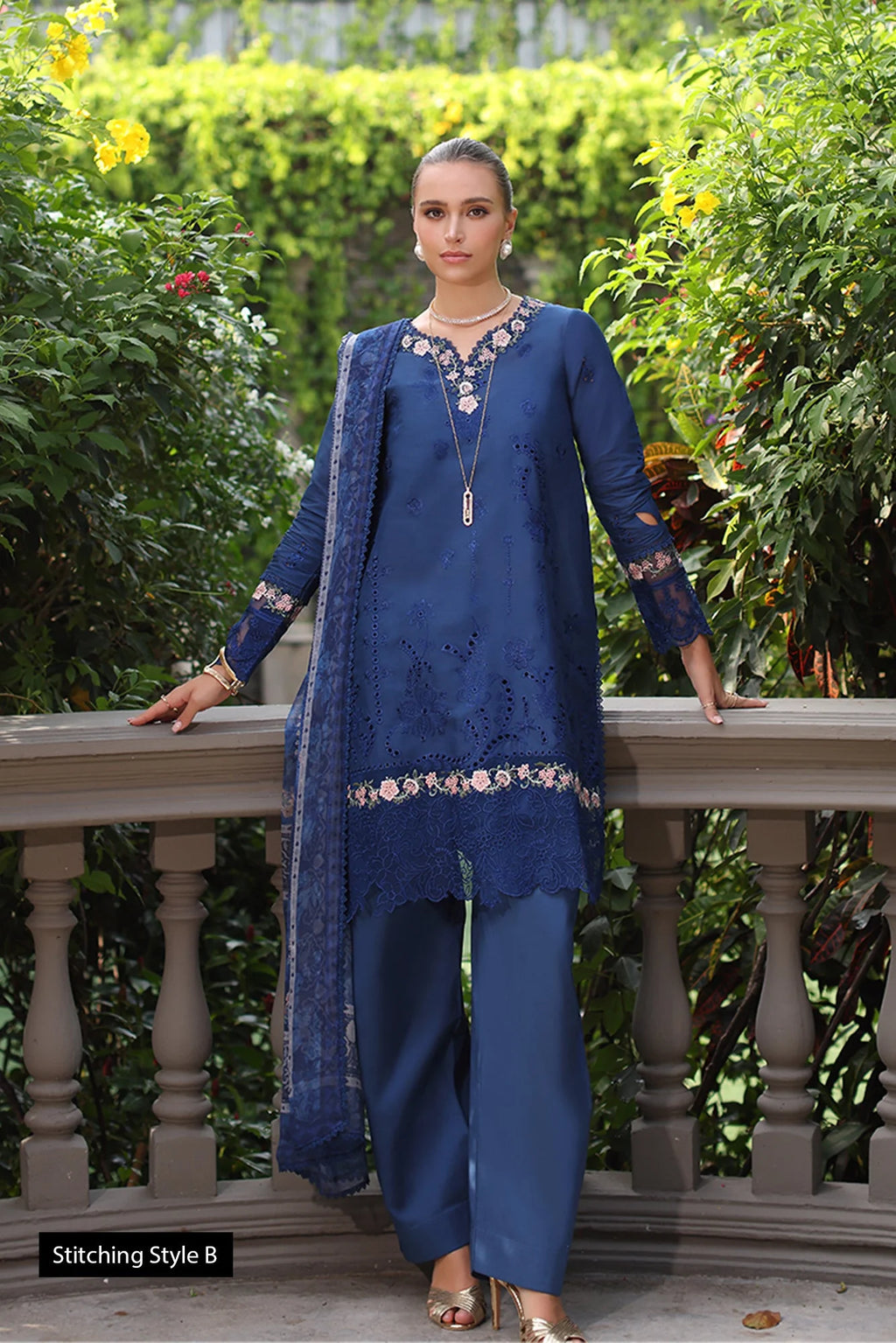 Woman in a blue traditional outfit standing outdoors with greenery in the background