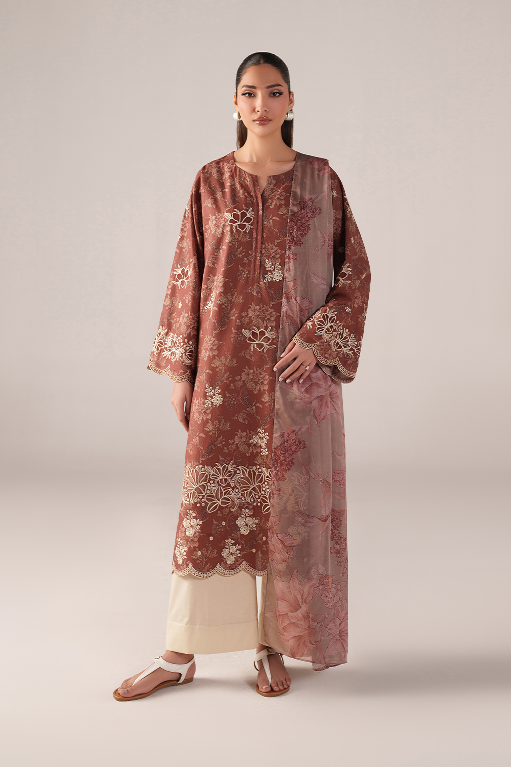 Woman wearing a long, patterned brown kurta with white pants on a plain background