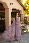 Woman in a lavender traditional outfit standing outdoors with a building and car in the background.