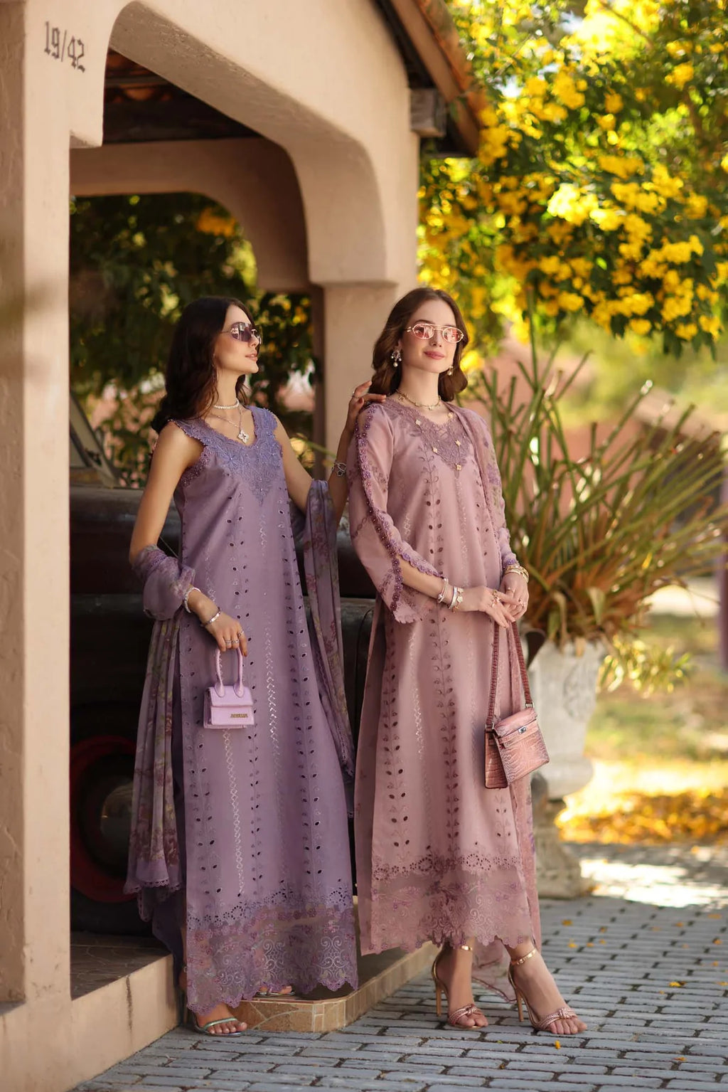 Two women in traditional attire standing outdoors with a decorative background.