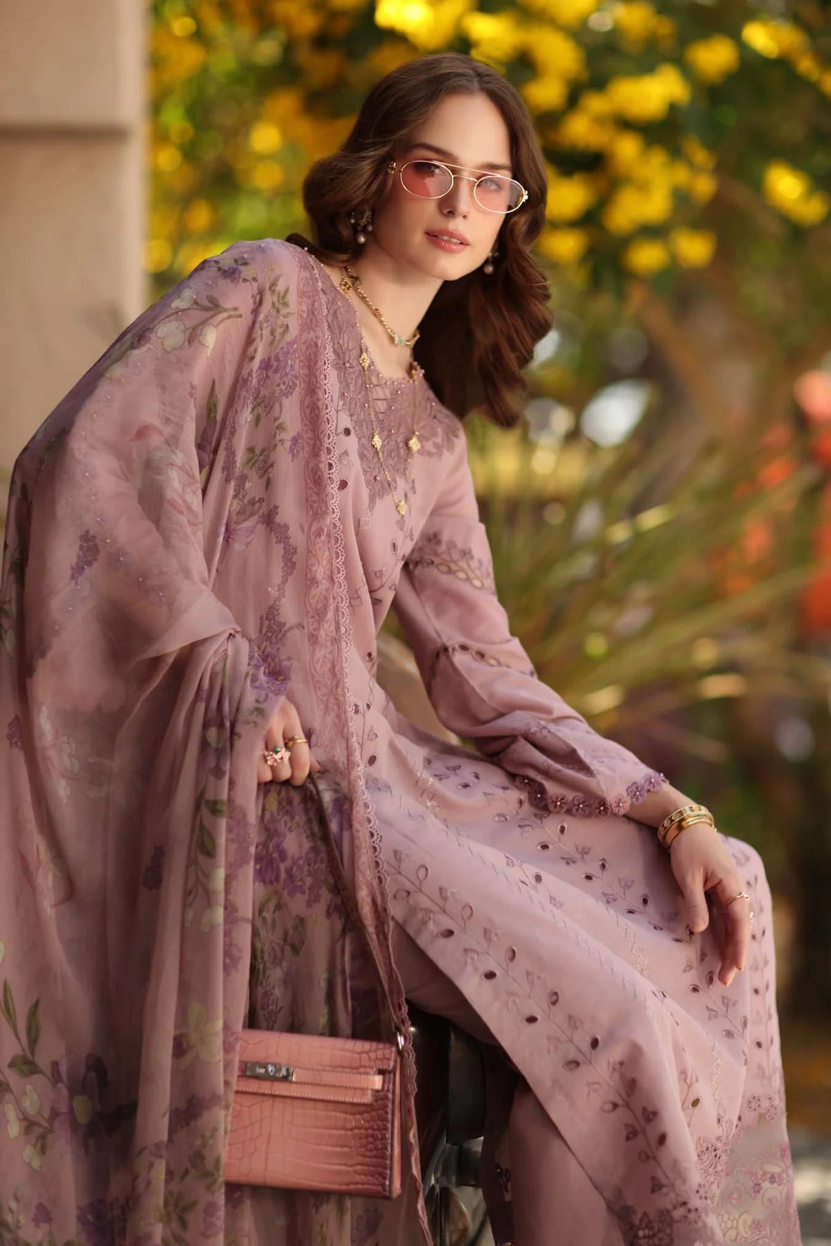 Woman in a floral dress with a matching shawl, holding a handbag, outdoors.
