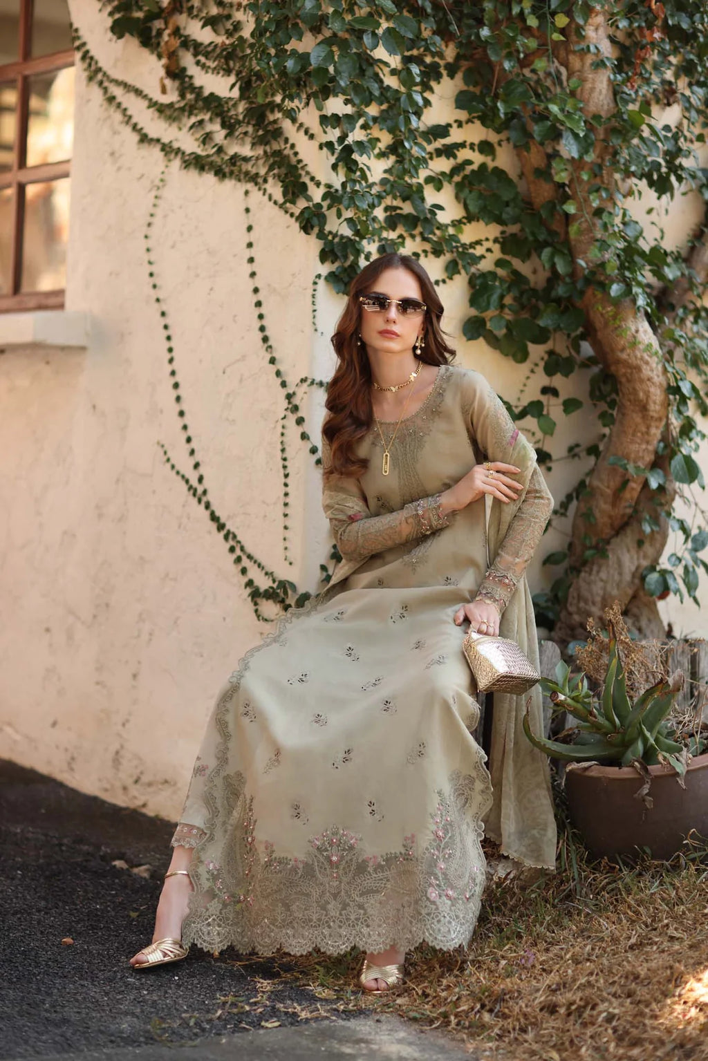 Woman in a light-colored saree sitting under a tree with greenery.