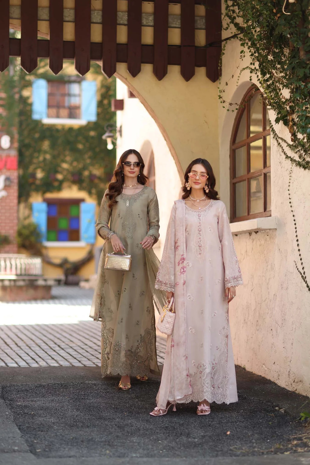 Two women in traditional outfits standing in front of a building with decorative elements.