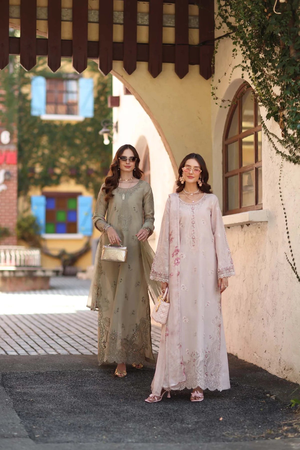 Two women in traditional outfits standing in front of a building with decorative elements.