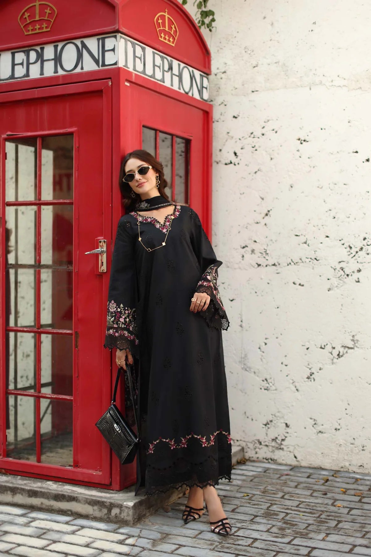 Woman in a black dress with floral embroidery standing next to a red telephone booth.