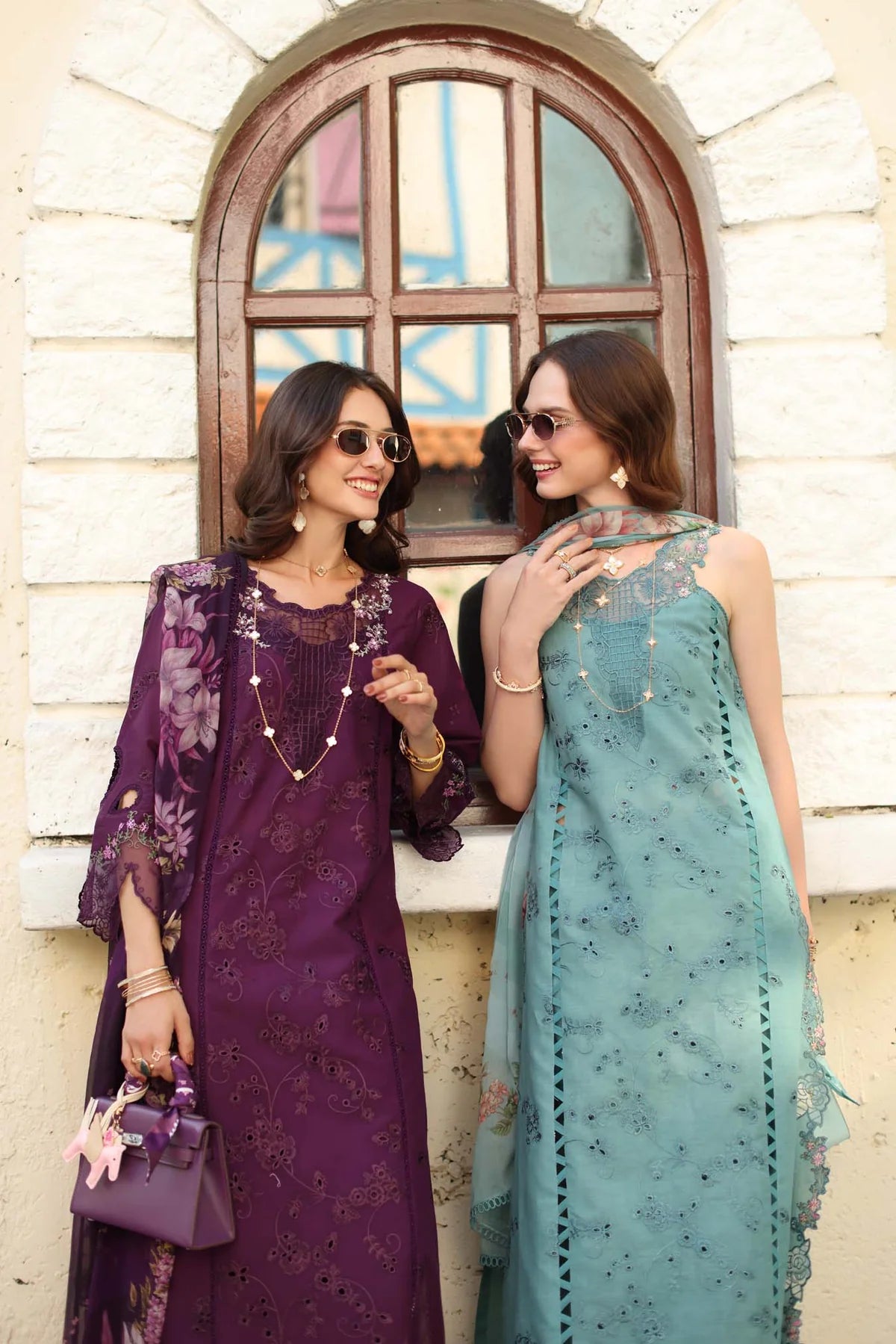 Two women in traditional outfits standing in front of a window.