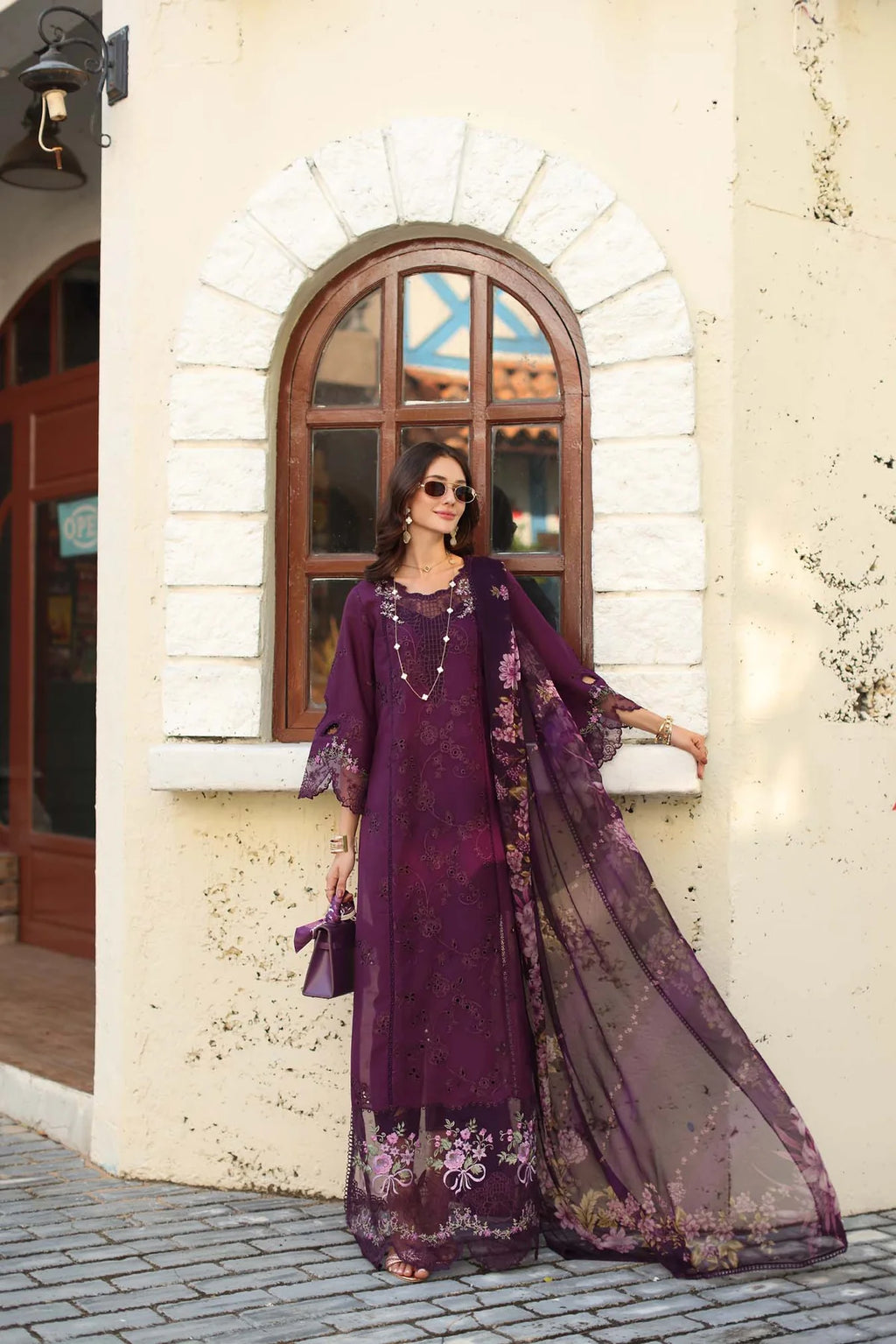 Woman in a long, dark purple embroidered dress standing in front of a stone building.