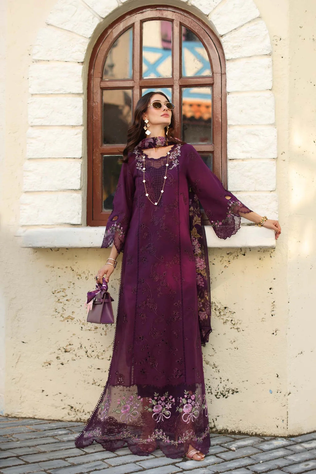 Woman in a purple embroidered dress standing in front of a stone building with an arched window.