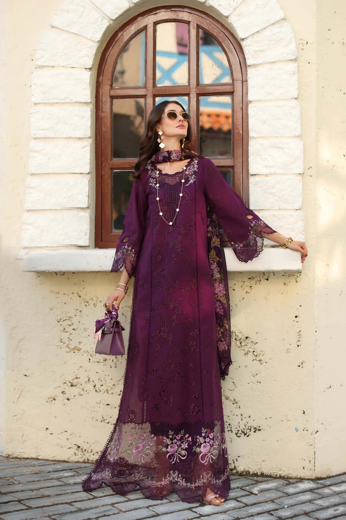 Woman in a purple embroidered dress standing in front of a stone building with an arched window.