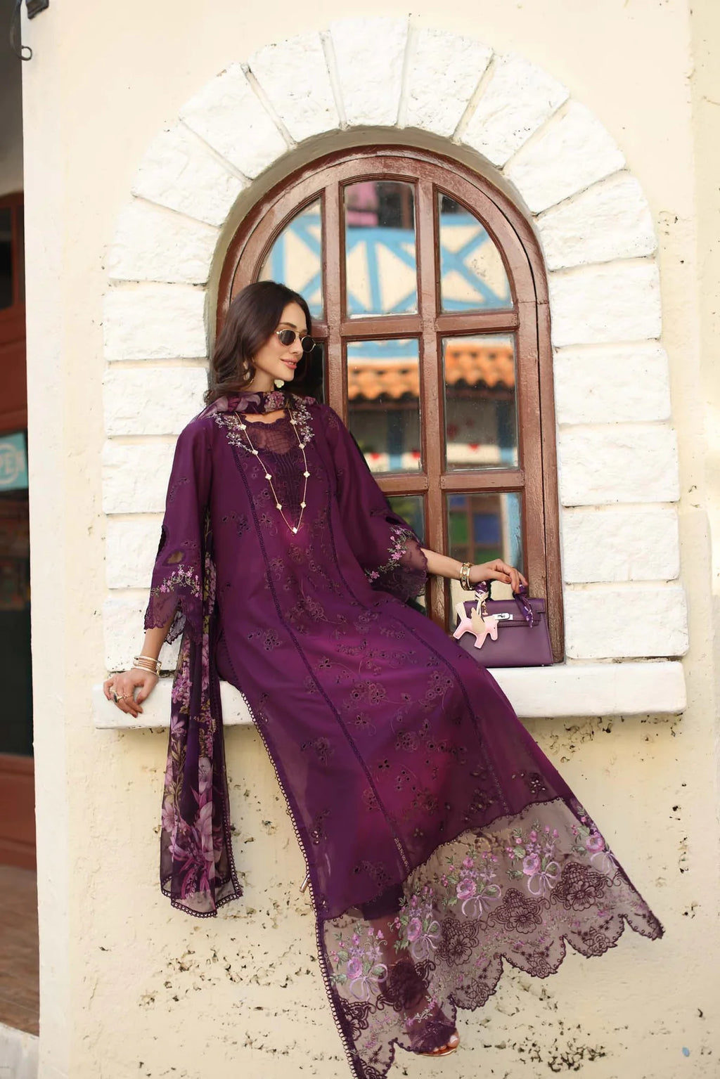 Woman in a purple dress with floral patterns sitting against a white wall with an archway.