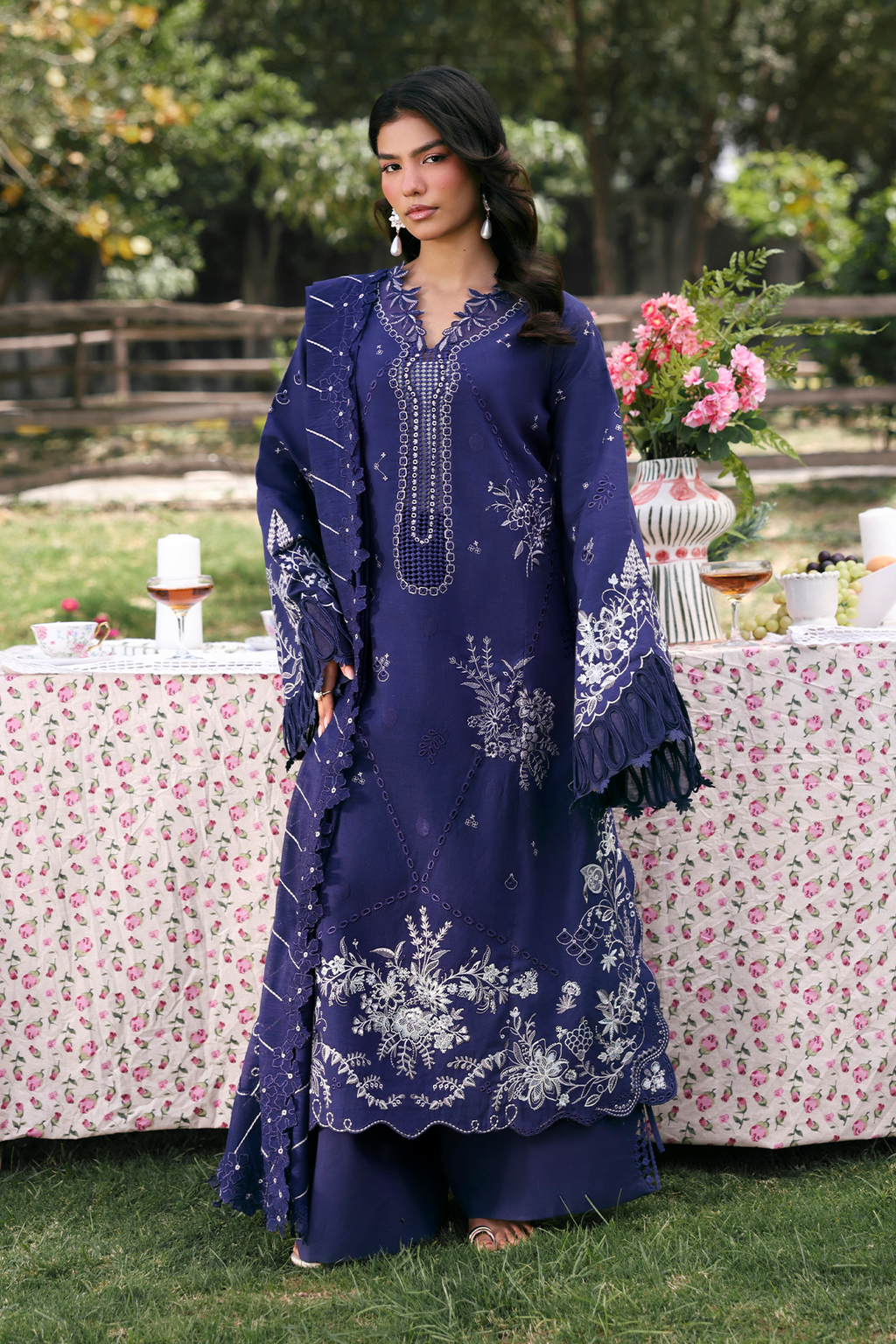 Woman in a blue embroidered dress standing outdoors with floral decorations.