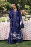 Woman in a blue embroidered dress standing outdoors with floral decorations.