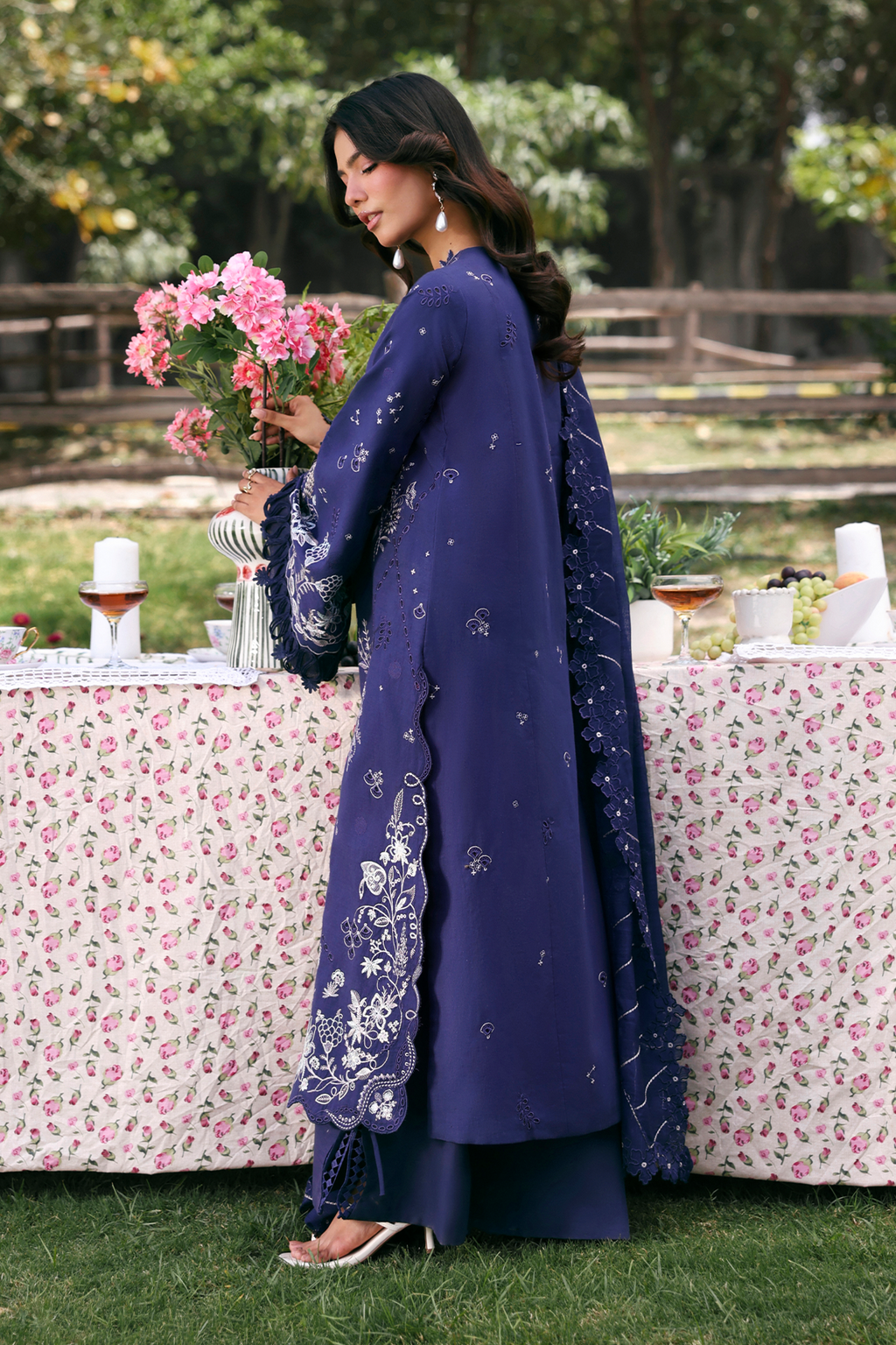 Woman in a blue traditional outfit holding flowers in a garden setting