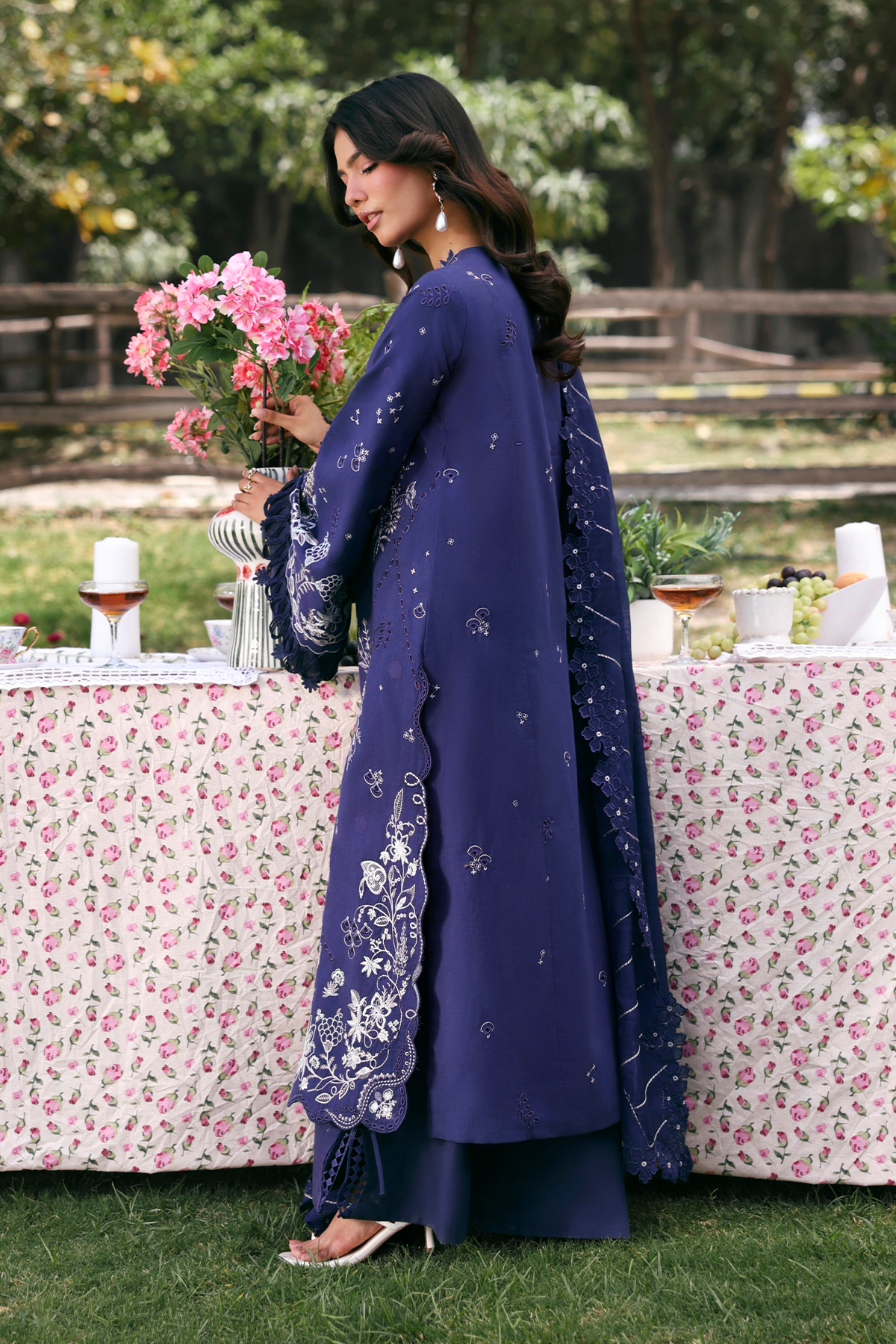 Woman in a blue traditional outfit holding flowers in a garden setting