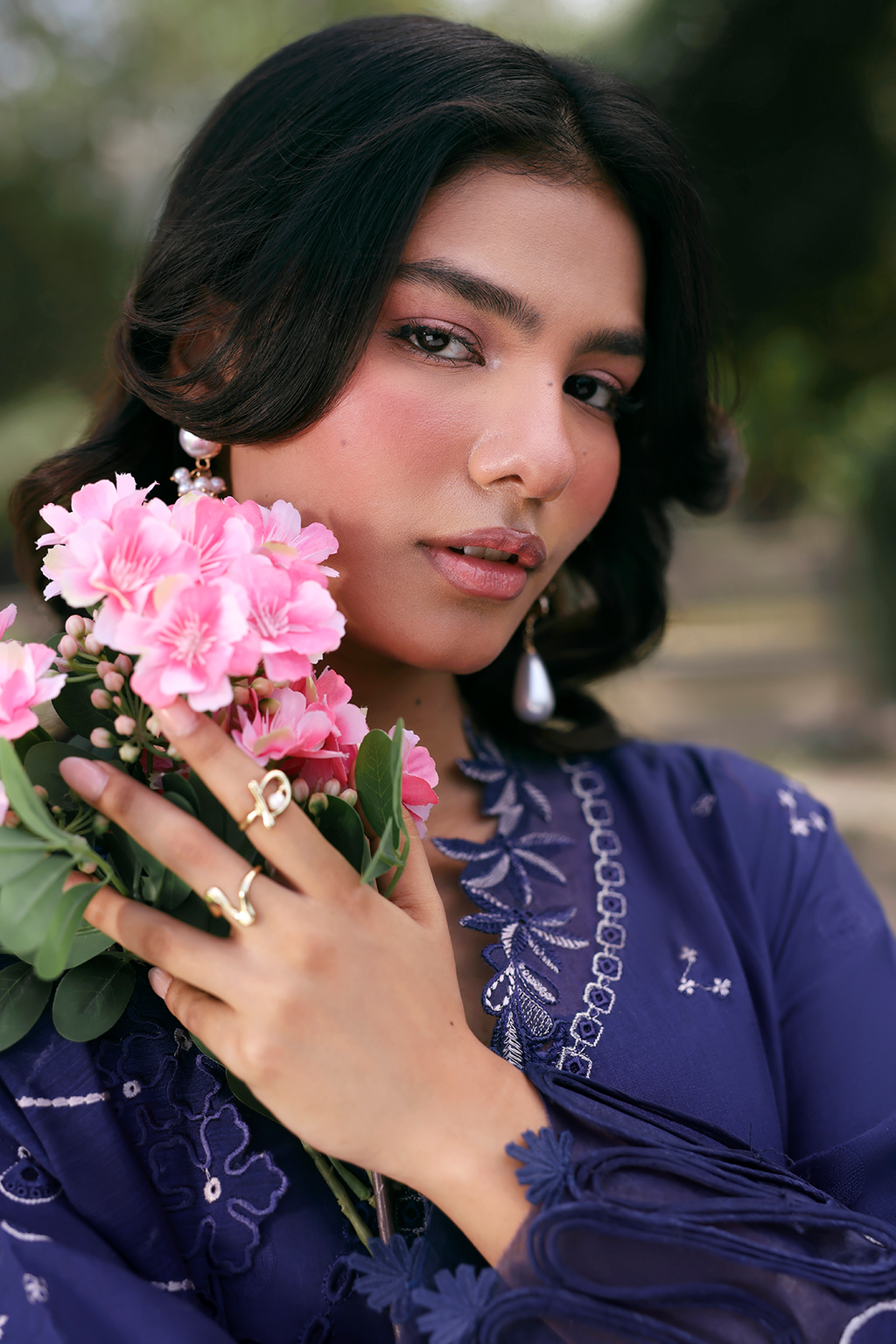 Woman holding pink flowers wearing a blue embroidered outfit outdoors