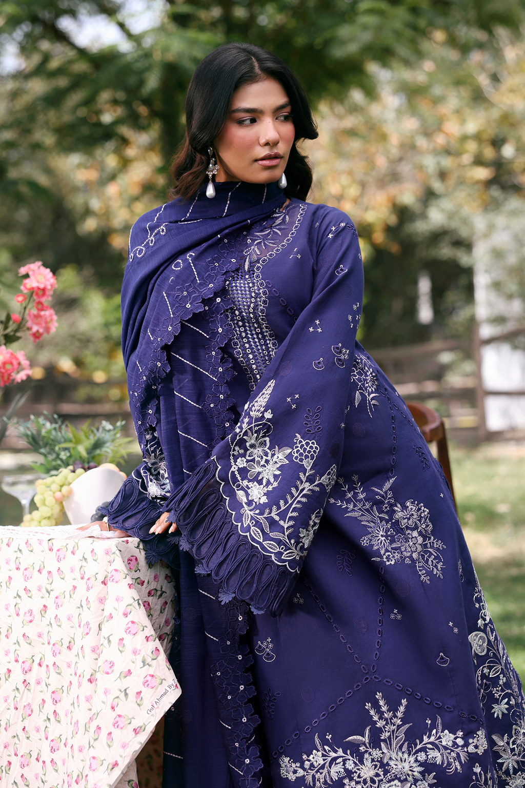 Woman wearing a blue embroidered traditional outfit outdoors with greenery in the background