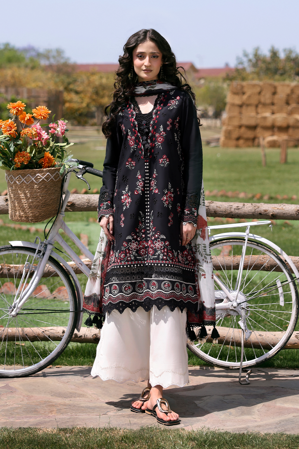 Woman in traditional attire standing next to a bicycle with flowers in a basket, outdoors.