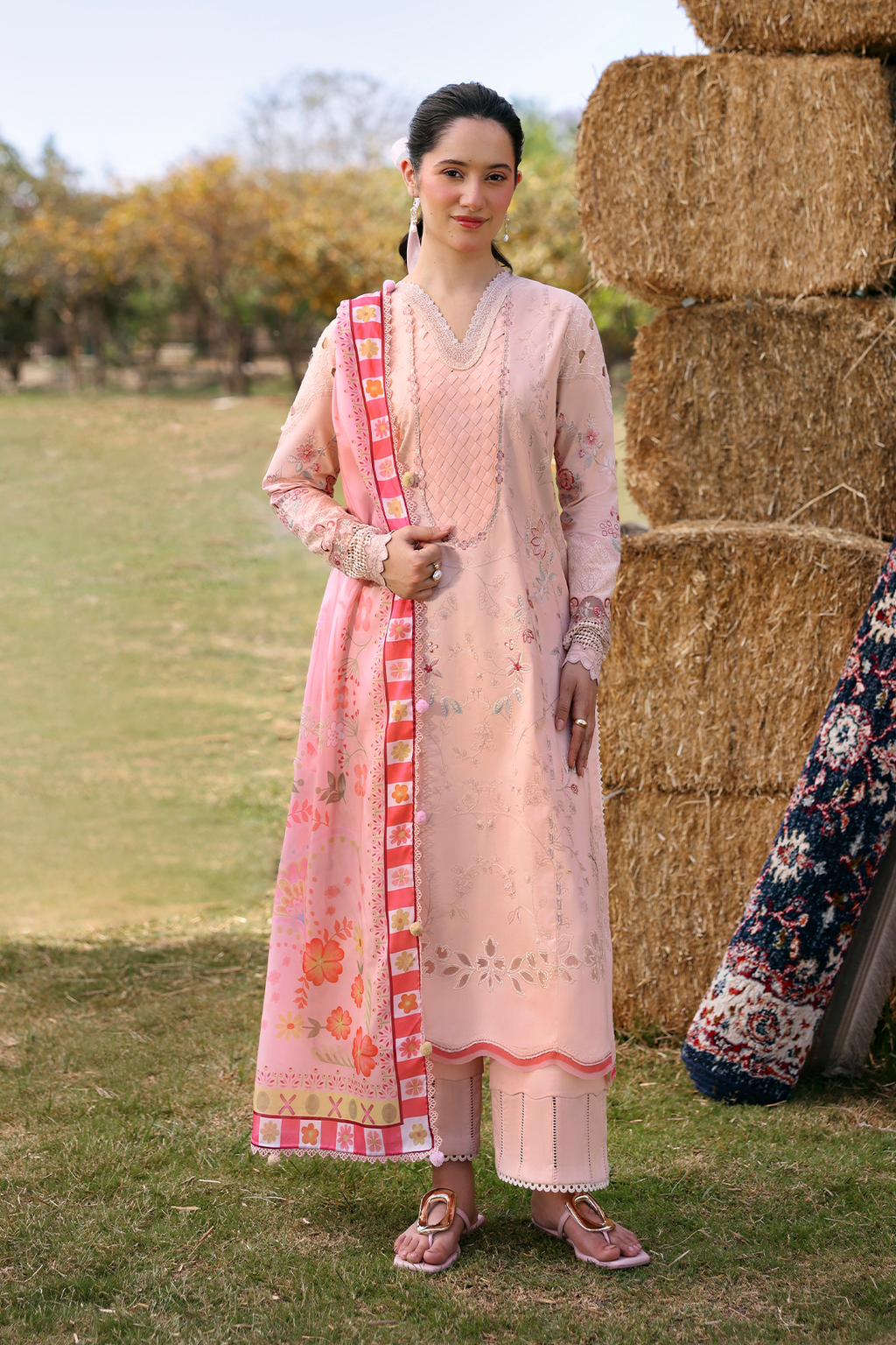 Woman in a traditional outfit standing next to hay bales outdoors