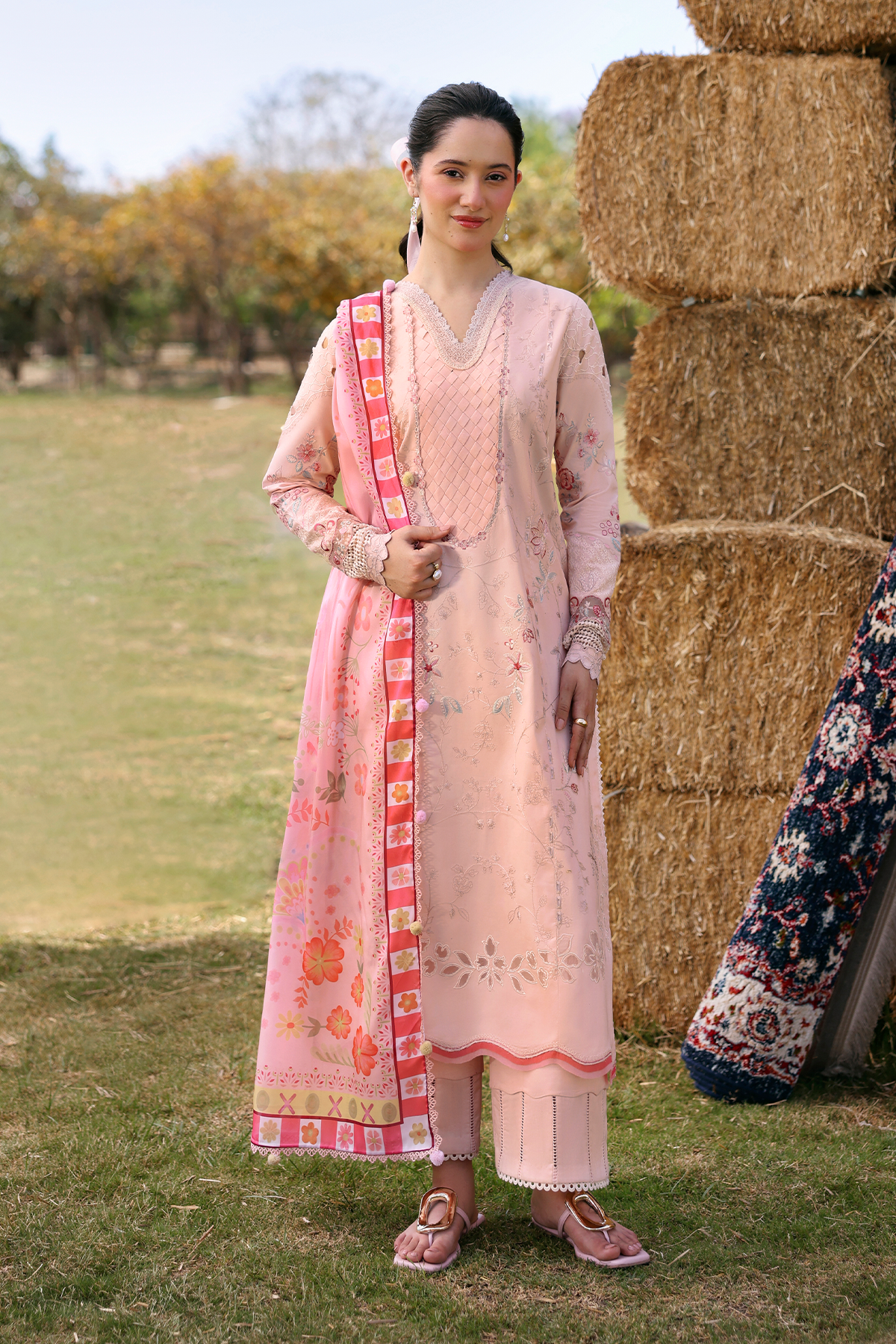 Woman in a traditional outfit standing next to hay bales outdoors