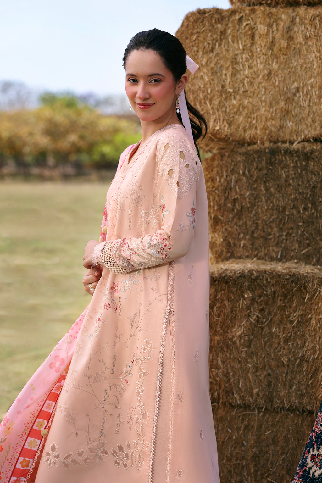 Woman in a peach embroidered dress standing next to hay bales outdoors