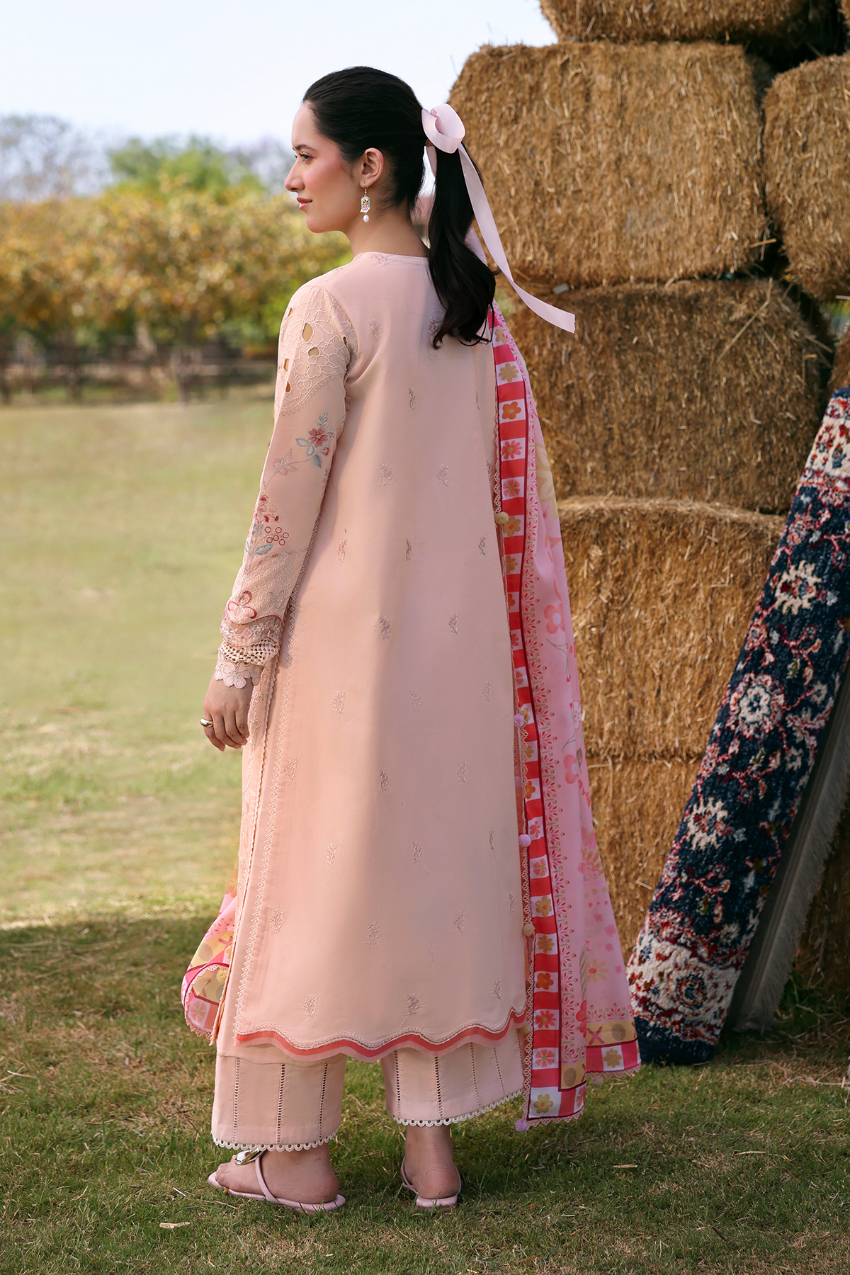 Woman in a traditional outfit standing next to hay bales in an outdoor setting