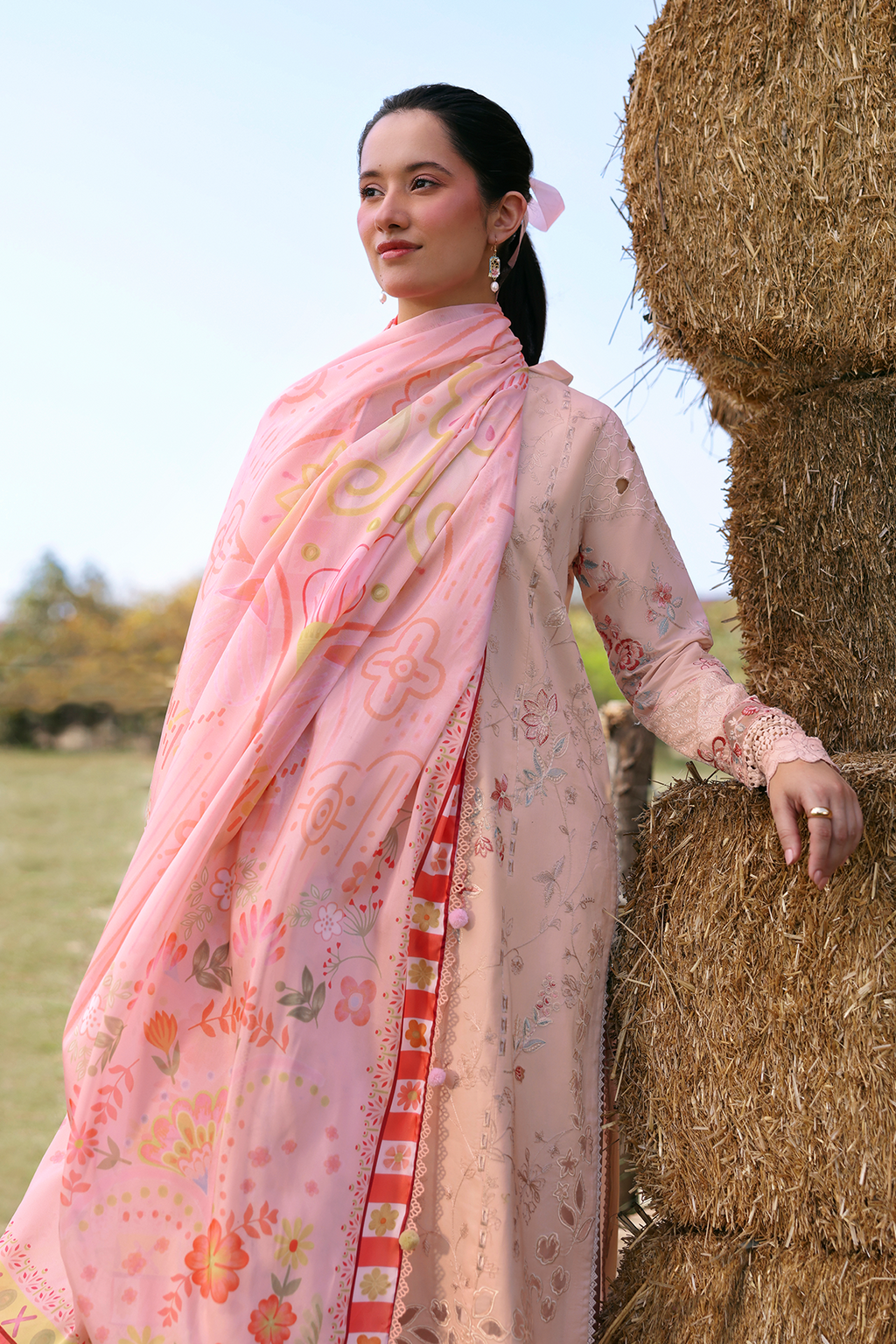Woman in a pink floral dress standing next to a hay bale outdoors