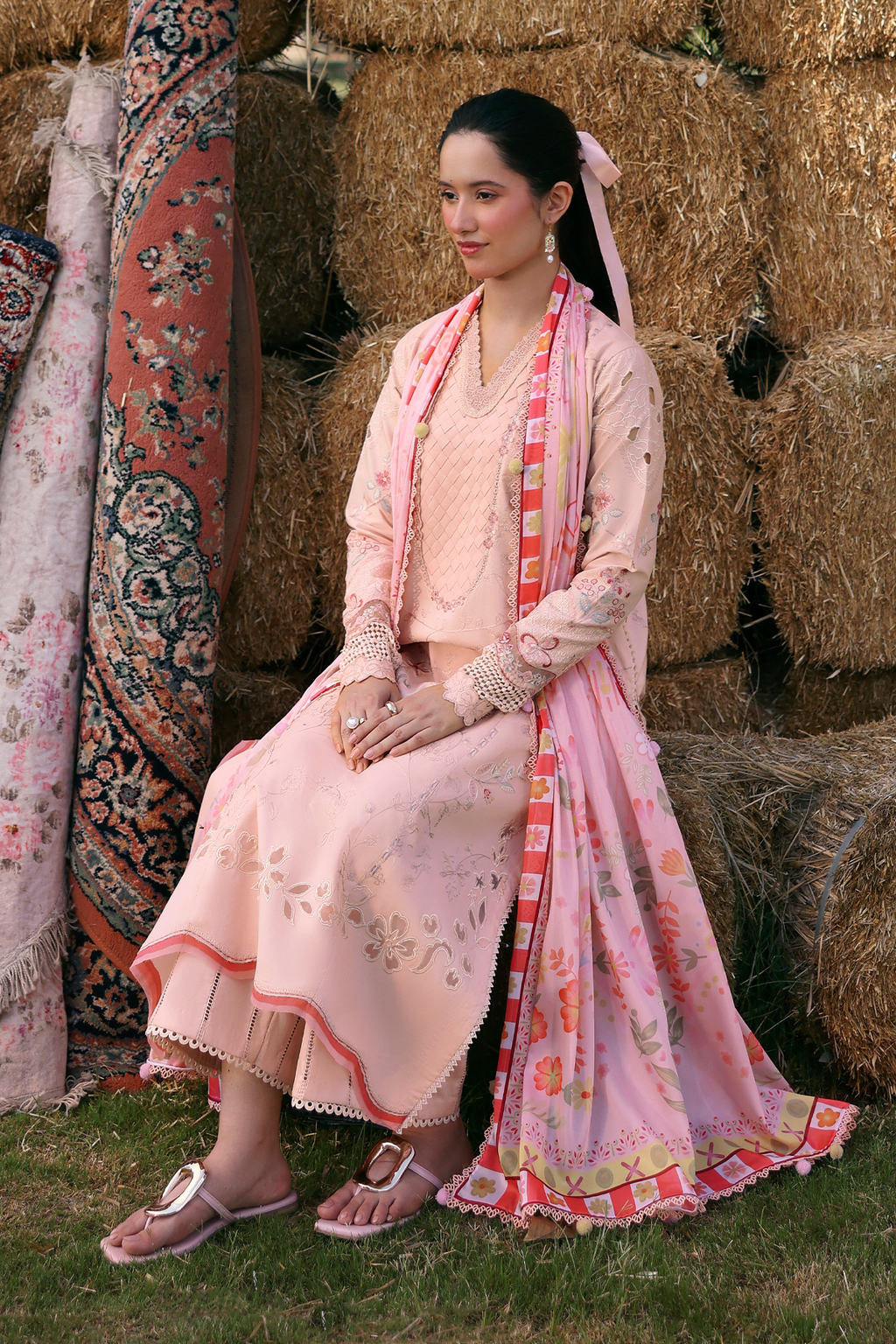 Woman in a traditional pink outfit sitting on hay bales with patterned fabric in the background