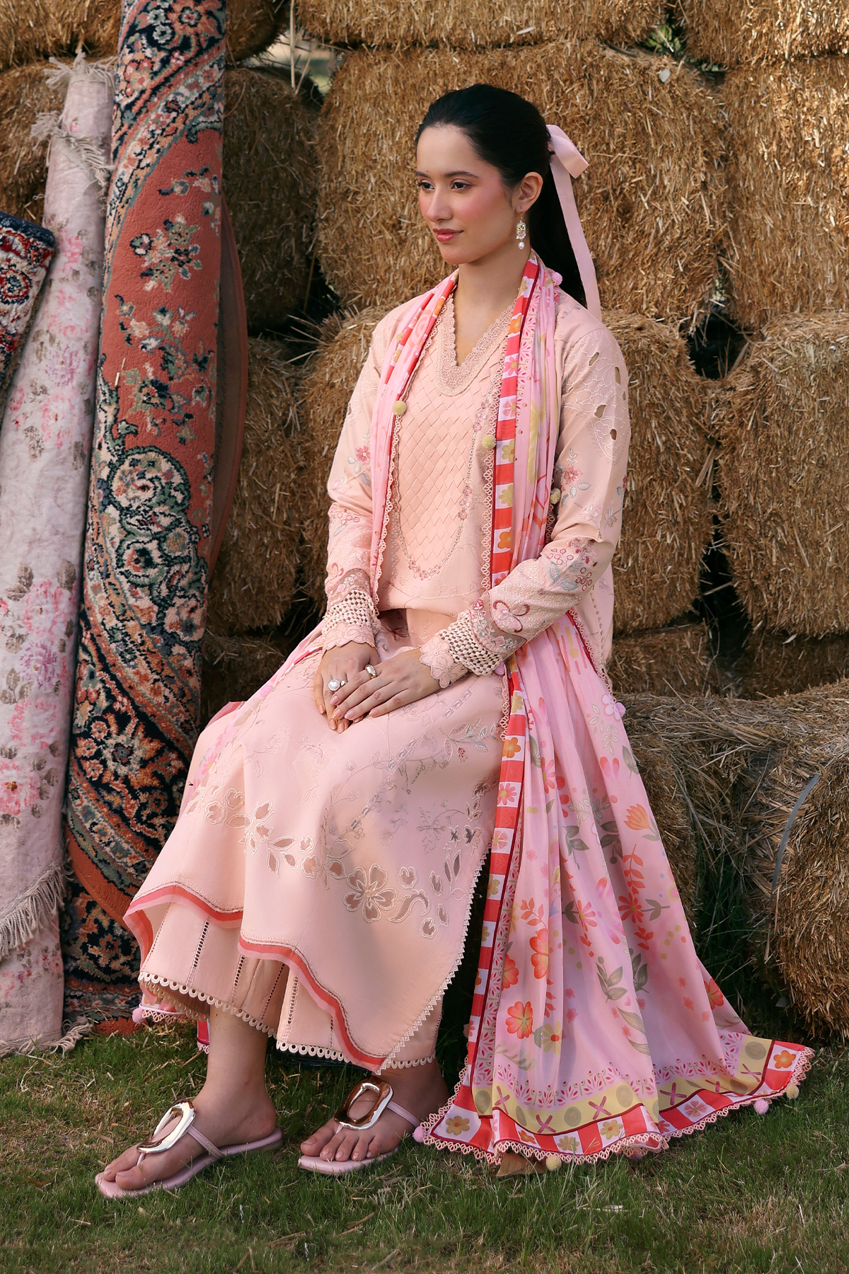 Woman in a traditional pink outfit sitting on hay bales with patterned fabric in the background