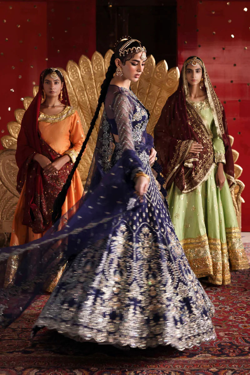 Woman in a blue embroidered dress with two other women in colorful traditional attire against a red background.