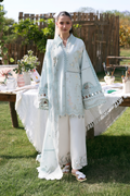 Woman in a light blue embroidered outfit standing outdoors with a table and plants in the background