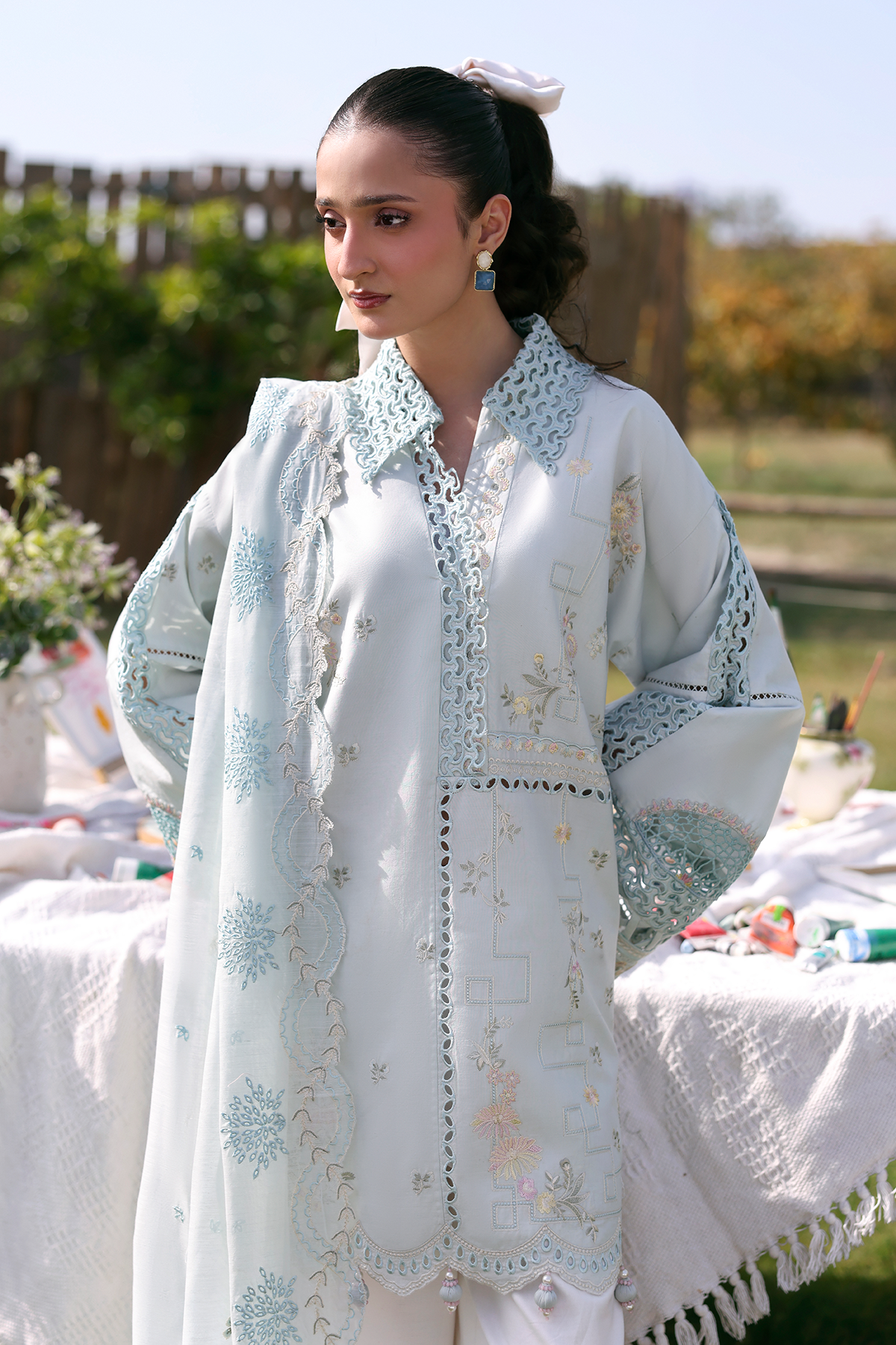 Woman wearing a light blue embroidered traditional outfit outdoors.