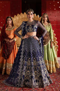 Woman in traditional embroidered outfit with two other women in colorful attire against a red wall.