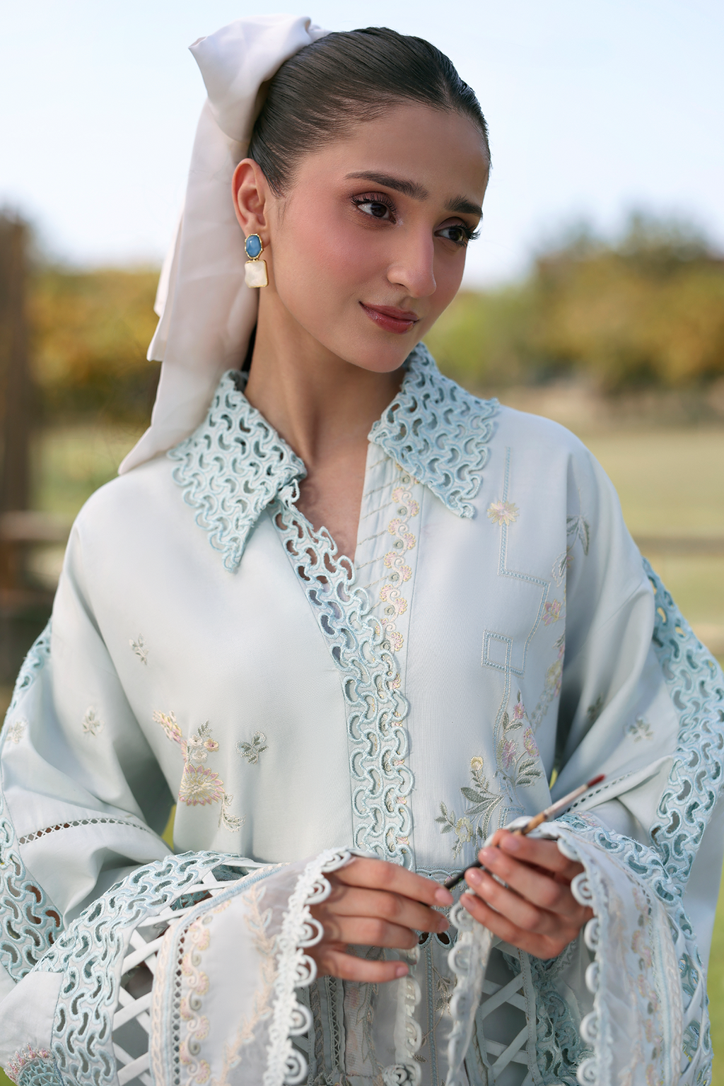 Woman in traditional light blue embroidered outfit with white headscarf outdoors