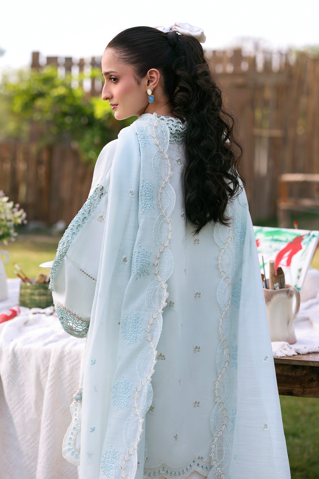 Woman wearing a light blue embroidered traditional outfit with a matching dupatta, standing outdoors.
