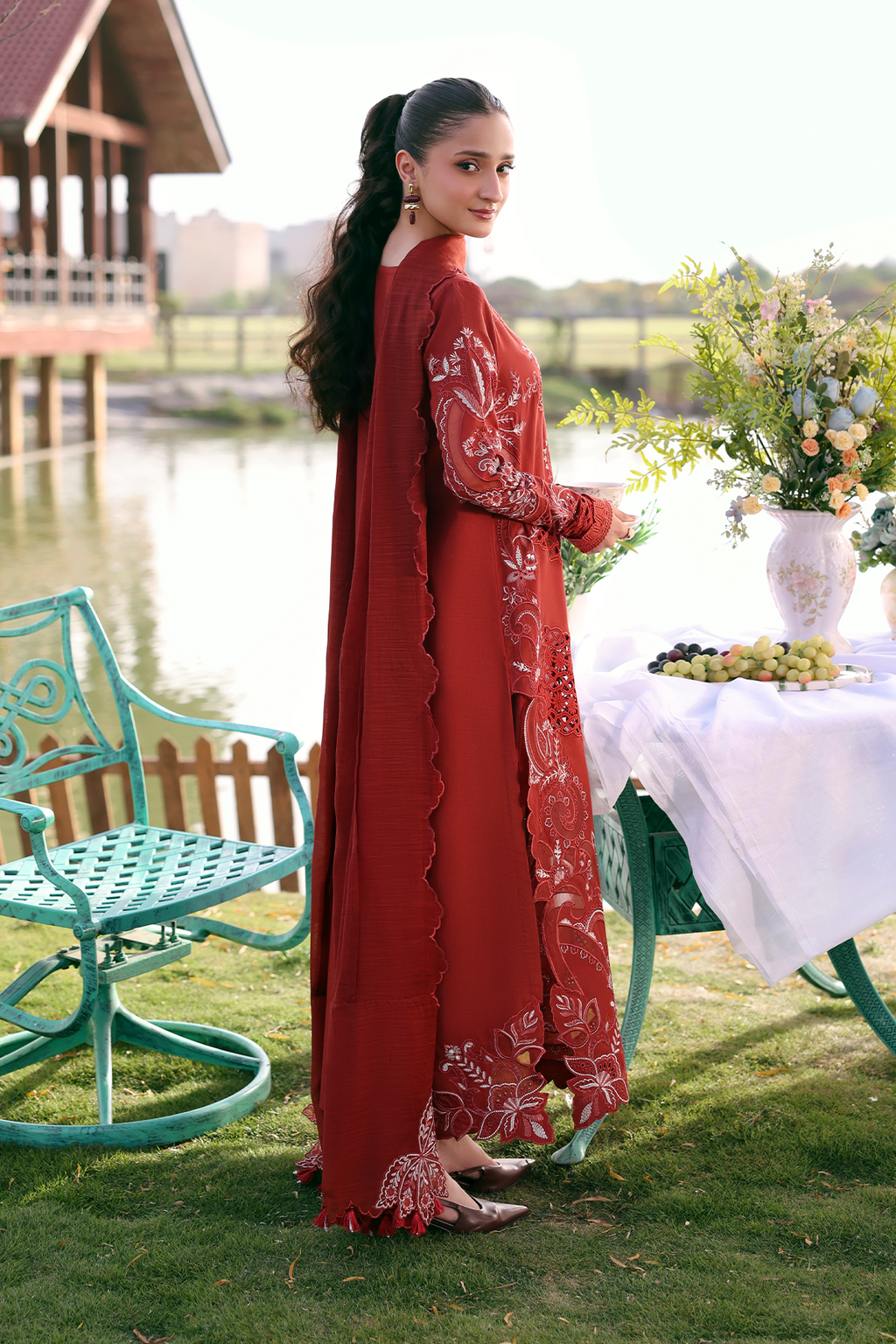 Woman in a red dress standing by a table outdoors near a body of water.