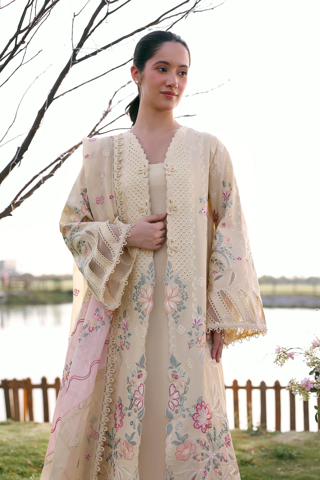 Woman wearing a floral kimono-style garment outdoors by a body of water.