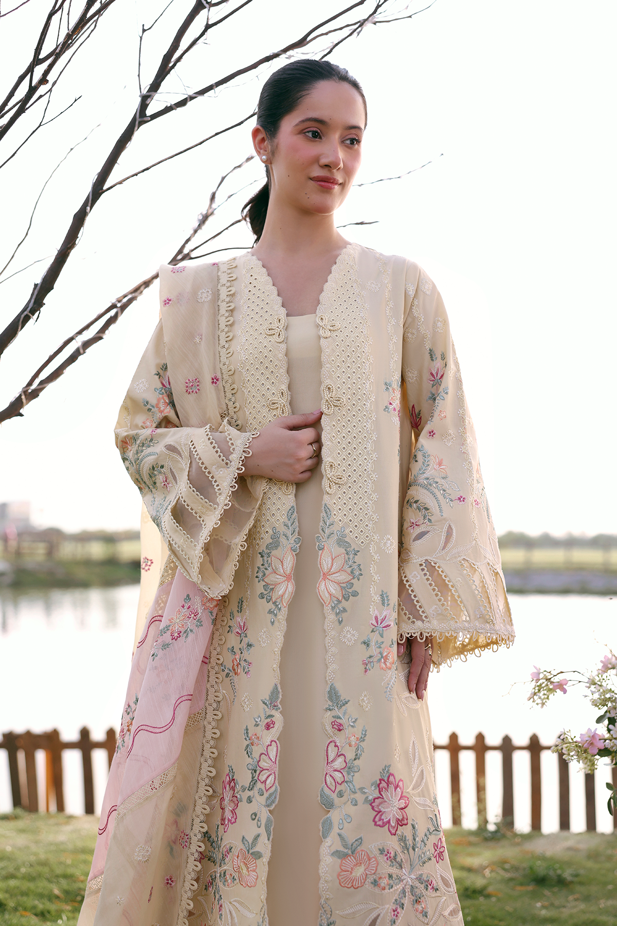 Woman wearing a floral kimono-style garment outdoors by a body of water.