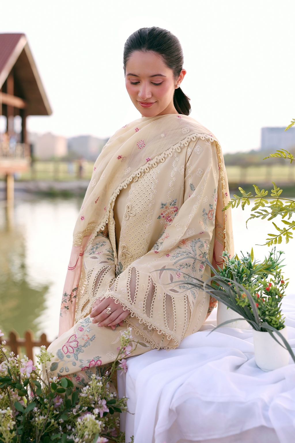 Woman in a traditional outfit with floral patterns sitting by a body of water.